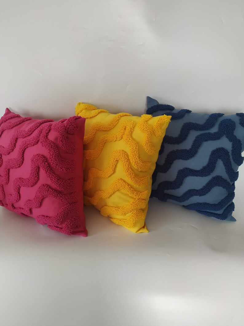 May include: Three decorative throw pillows with a wavy pattern. The pillows are pink, yellow, and blue.