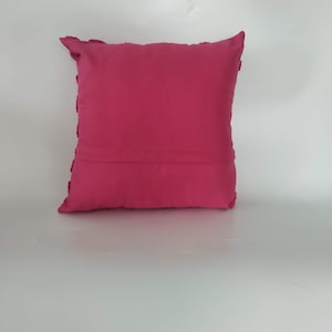 May include: A pink throw pillow with a textured border. The pillow is made of a soft, plush fabric.