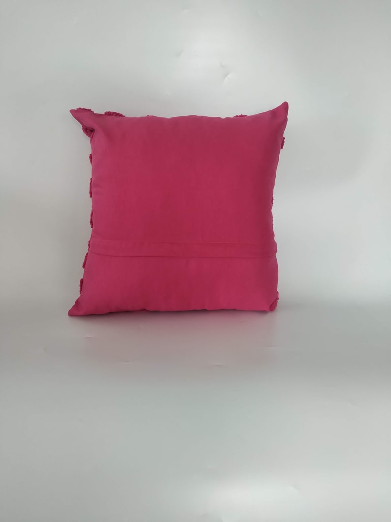 May include: A pink throw pillow with a textured border. The pillow is made of a soft, plush fabric.