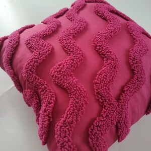 May include: A pink throw pillow with a textured, wavy pattern. The pillow is made of a soft, plush fabric.