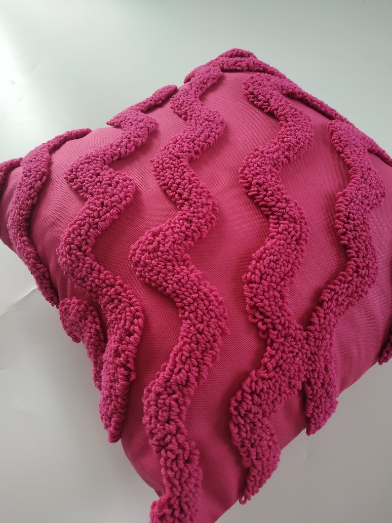 May include: A pink throw pillow with a textured, wavy pattern. The pillow is made of a soft, plush fabric.
