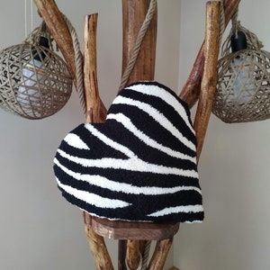 May include: A black and white zebra patterned heart-shaped cushion sits on a wooden stand with rope accents. The stand has two hanging light fixtures with woven shades.