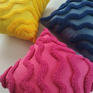 May include: Three decorative throw pillows with a wavy pattern. The pillows are yellow, blue, and pink.