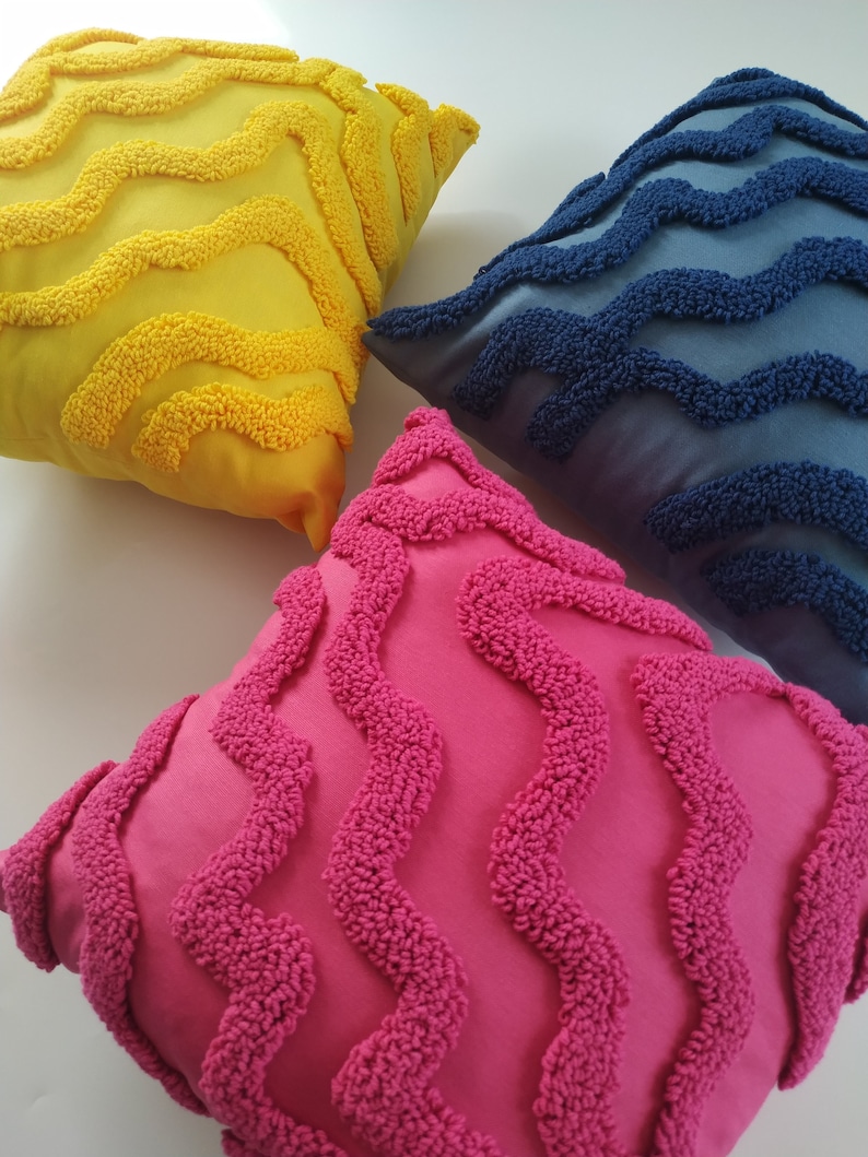 May include: Three decorative throw pillows with a wavy pattern. The pillows are yellow, blue, and pink.