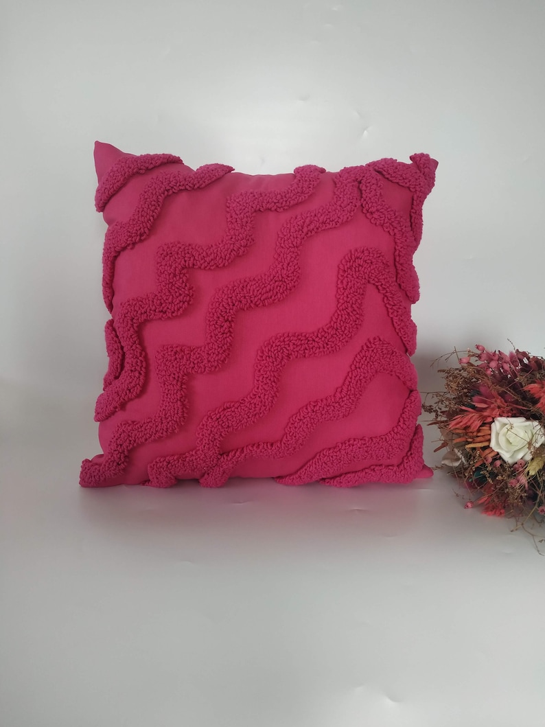 May include: A pink throw pillow with a textured wave pattern. The pillow is made of a soft, plush fabric.