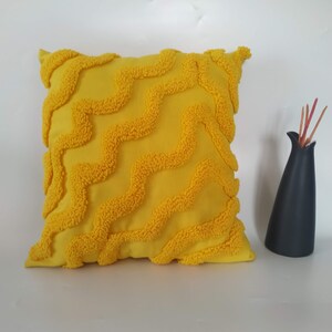 May include: A yellow throw pillow with a textured, wavy pattern. The pillow is made of a soft, plush fabric.