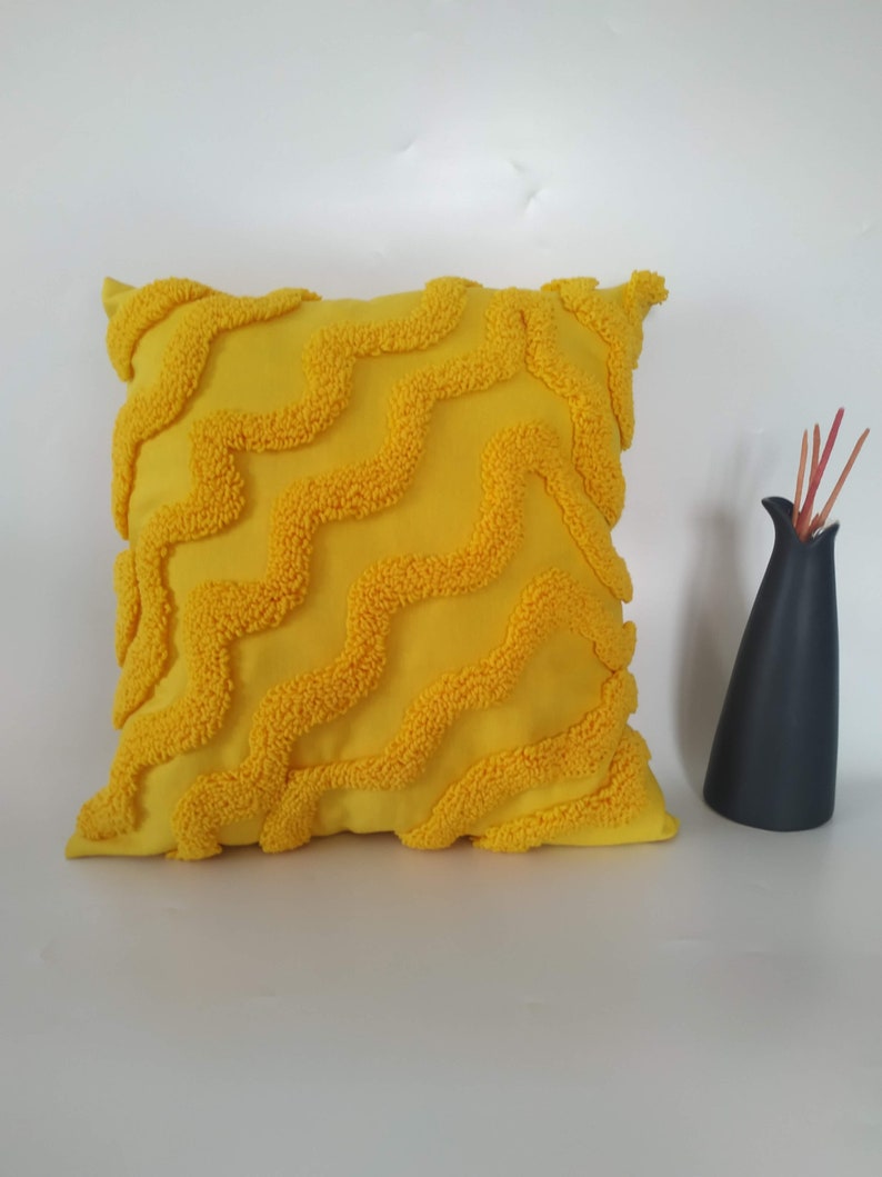 May include: A yellow throw pillow with a textured, wavy pattern. The pillow is made of a soft, plush fabric.