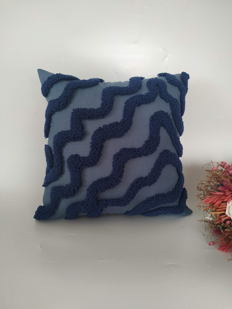 May include: A blue throw pillow with a textured, wavy pattern. The pillow is made of a soft, plush fabric.