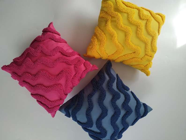 May include: Three decorative throw pillows with a wavy, textured design. The pillows are pink, yellow, and blue.