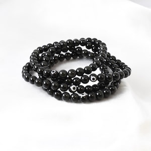 May include: A stack of black beaded bracelets with a white evil eye charm on each bead.