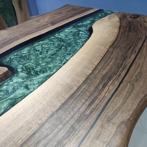 May include: A wooden table top with a green epoxy river running through it. The wood is a dark brown with black lines running through it.