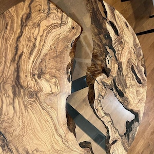 May include: A round wooden table top with a natural wood grain pattern. The table top has a clear epoxy resin fill with a unique river pattern. The table top is approximately 40 inches in diameter.