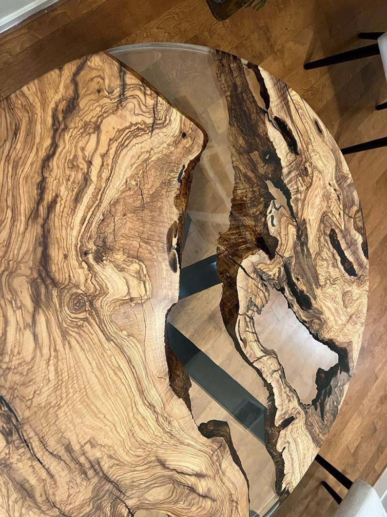 May include: A round wooden table top with a natural wood grain pattern. The table top has a clear epoxy resin fill with a unique river pattern. The table top is approximately 40 inches in diameter.