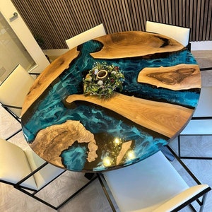 May include: A round wooden dining table with a blue and black epoxy resin inlay. The table is surrounded by white chairs with black metal frames.