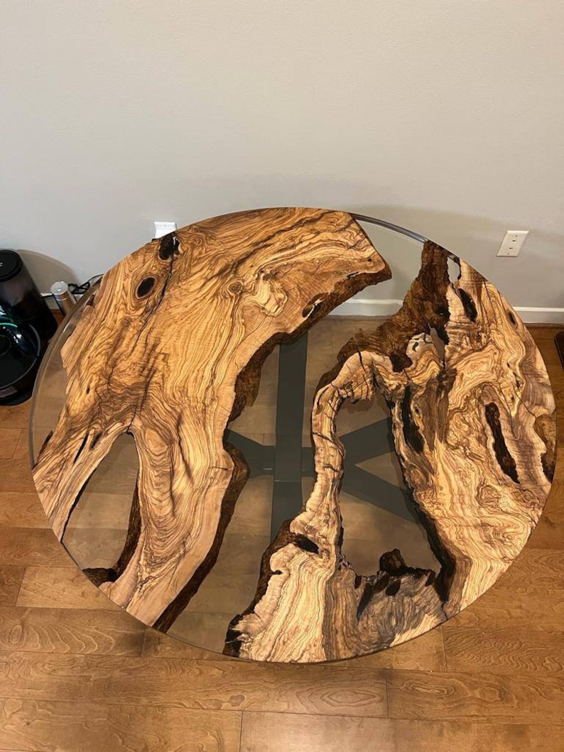 May include: A round wooden table top with a natural wood grain pattern and a clear epoxy resin fill. The table top is set on a black metal base.