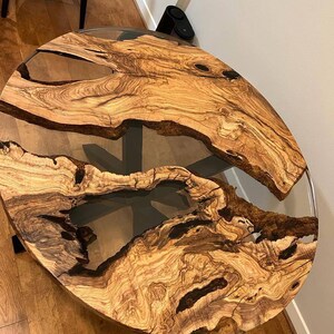 May include: Round wooden table top with a clear epoxy resin fill. The wood has a natural brown and black grain pattern.