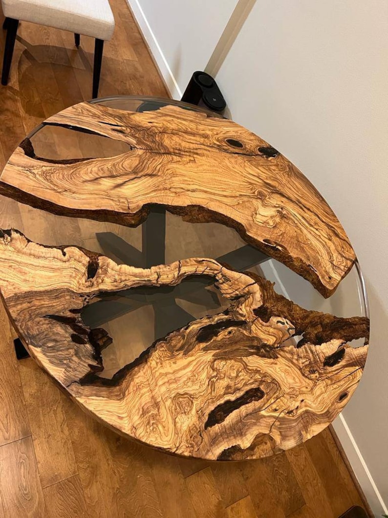 May include: Round wooden table top with a clear epoxy resin fill. The wood has a natural brown and black grain pattern.