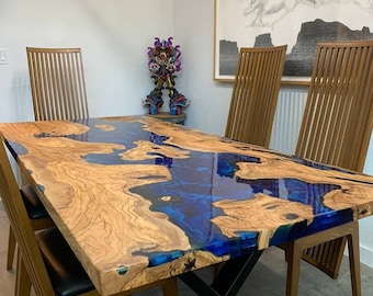 Pode incluir: Uma mesa de jantar de madeira com uma incrustação de resina epóxi azul. A mesa tem uma base de metal preto em forma de X e é rodeada por cadeiras de madeira com assentos de couro preto.