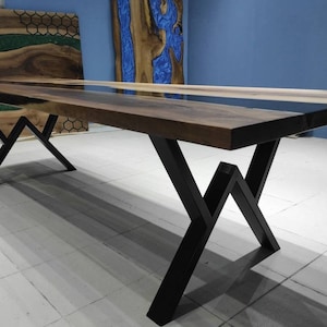 May include: A long wooden dining table with a black epoxy resin inlay. The table has a black metal base with a geometric design.
