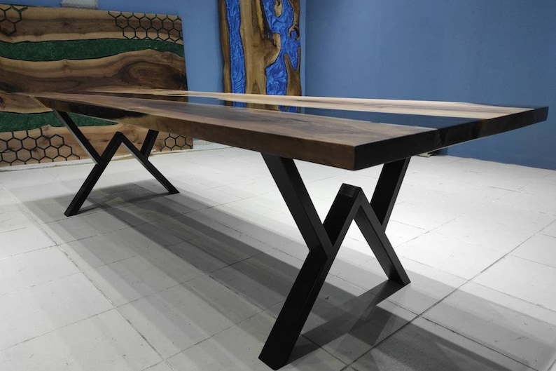 May include: A long wooden dining table with a black epoxy resin inlay. The table has a black metal base with a geometric design.