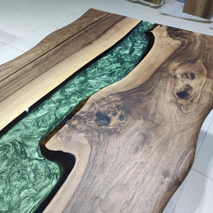 May include: A wooden table top with a live edge design. The table top has a green epoxy river running through the center.
