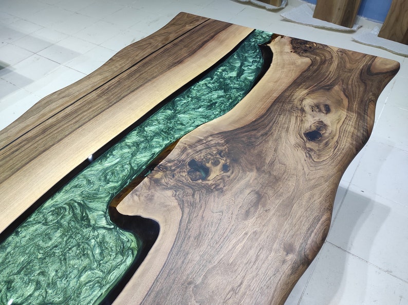 May include: A wooden table top with a live edge design. The table top has a green epoxy river running through the center.