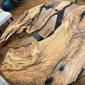 May include: A round wooden table top with a natural wood grain pattern and a clear epoxy resin fill. The table top has a dark brown and black color scheme.