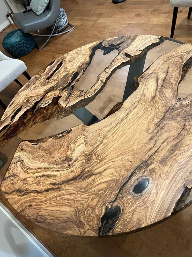 May include: A round wooden table top with a natural wood grain pattern and a clear epoxy resin fill. The table top has a dark brown and black color scheme.