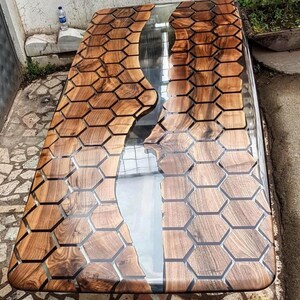 Puede incluir: Una mesa de madera con un r&iacute;o de resina epoxi transparente que recorre el centro. La madera es de color marr&oacute;n oscuro y tiene un patr&oacute;n de panal. La resina es transparente y tiene un ligero efecto de ondulaci&oacute;n.