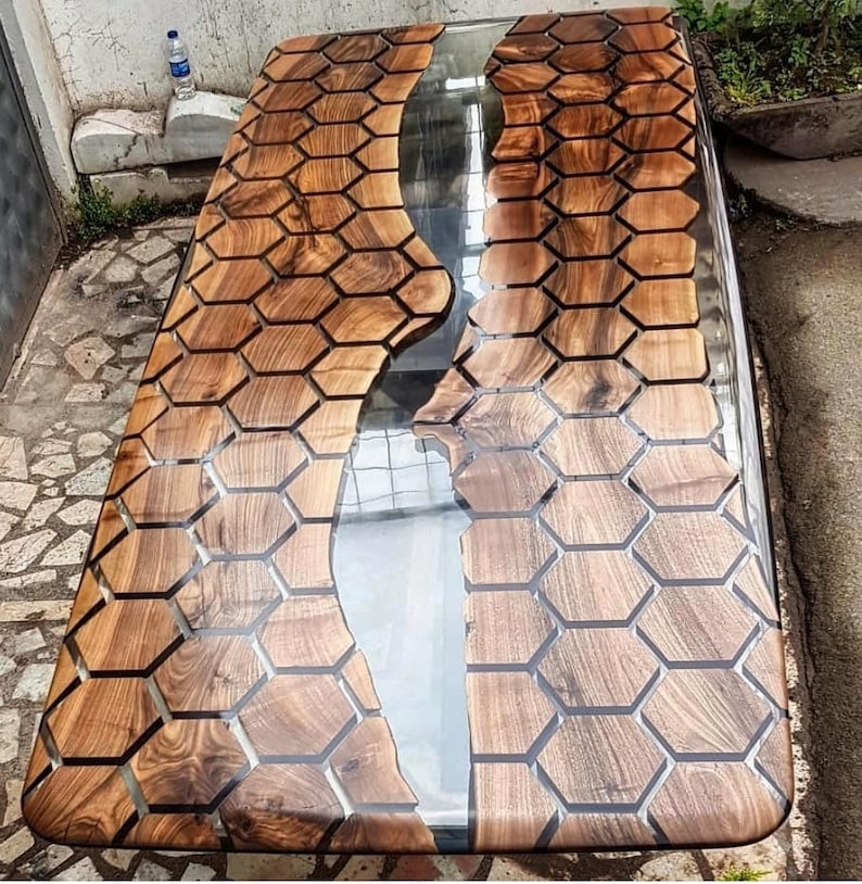 Puede incluir: Una mesa de madera con un r&iacute;o de resina epoxi transparente que recorre el centro. La madera es de color marr&oacute;n oscuro y tiene un patr&oacute;n de panal. La resina es transparente y tiene un ligero efecto de ondulaci&oacute;n.