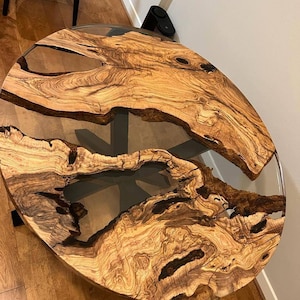 May include: A round wooden table top with a natural wood grain pattern and clear epoxy resin filling in the cracks. The table top is approximately 3 feet in diameter.