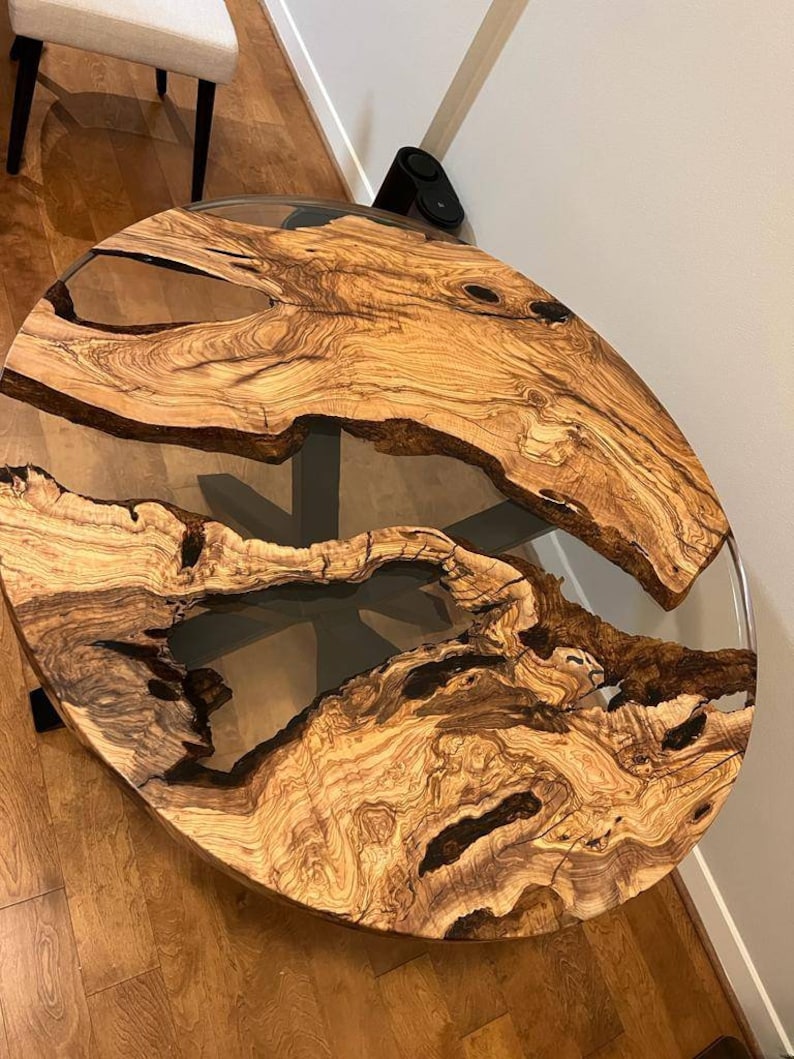 May include: A round wooden table top with a natural wood grain pattern and clear epoxy resin filling in the cracks. The table top is approximately 3 feet in diameter.