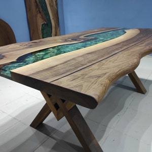 May include: A wooden table with a live edge top and a green epoxy river running through the center. The table is supported by a simple X-shaped base.