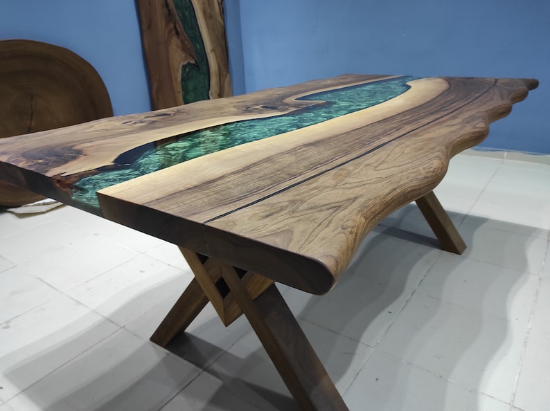 May include: A wooden table with a live edge top and a green epoxy river running through the center. The table is supported by a simple X-shaped base.
