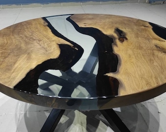 Könnte beinhalten: Eine runde Tischplatte aus Holz mit einem Design aus schwarzem und klarem Epoxidharz in Flussform. Der Tisch hat ein schwarzes Metallgestell.