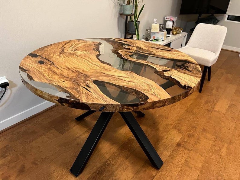 May include: Round wooden dining table with a clear epoxy resin top. The table has a natural wood grain pattern and black metal legs.