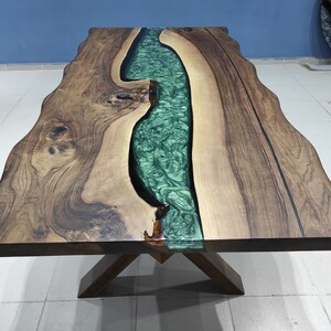 May include: A wooden table with a live edge and a green epoxy river running through the center. The table has a natural wood finish and a simple X-shaped base.