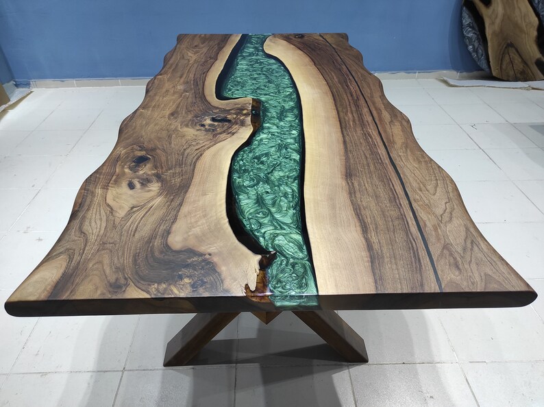May include: A wooden table with a live edge and a green epoxy river running through the center. The table has a natural wood finish and a simple X-shaped base.