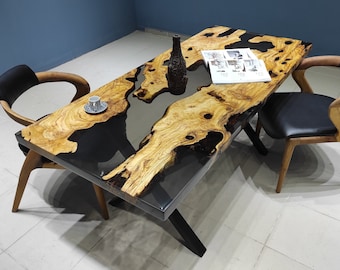 May include: A wooden dining table with a black epoxy resin inlay. The table has a natural wood grain and a live edge design. Two black leather chairs are placed around the table.