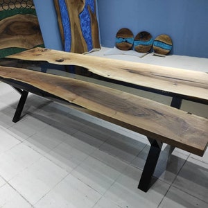 May include: A long, wooden dining table with a black epoxy resin inlay. The table has a black metal X-shaped base.