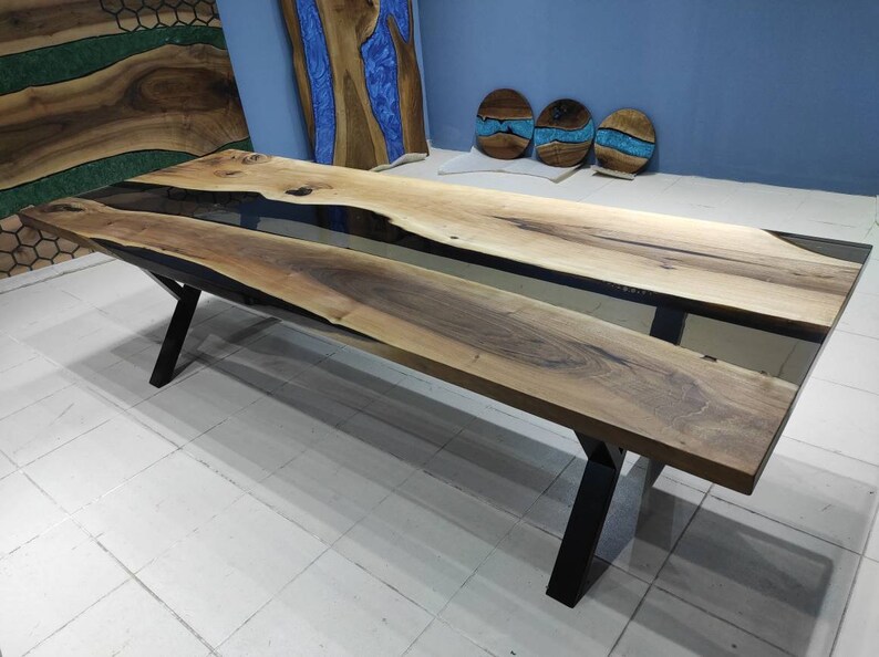 May include: A long, wooden dining table with a black epoxy resin inlay. The table has a black metal X-shaped base.