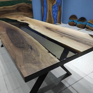 May include: A long, rectangular wooden table with a black epoxy river running down the center. The table has a black metal X-shaped base.
