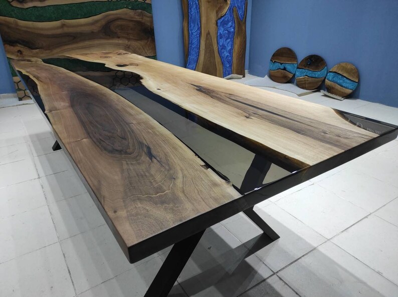 May include: A long, rectangular wooden table with a black epoxy river running down the center. The table has a black metal X-shaped base.