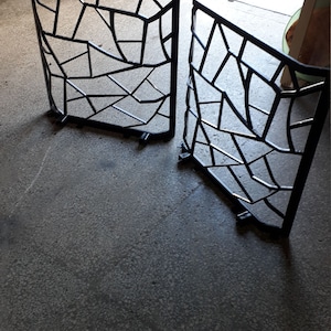 Puede incluir: Dos portales de metal negro con un dise&ntilde;o geom&eacute;trico. Los portales est&aacute;n hechos de finas barras de metal soldadas entre s&iacute; para crear un patr&oacute;n de cuadrados y tri&aacute;ngulos. Los portales est&aacute;n sobre un suelo de hormig&oacute;n.
