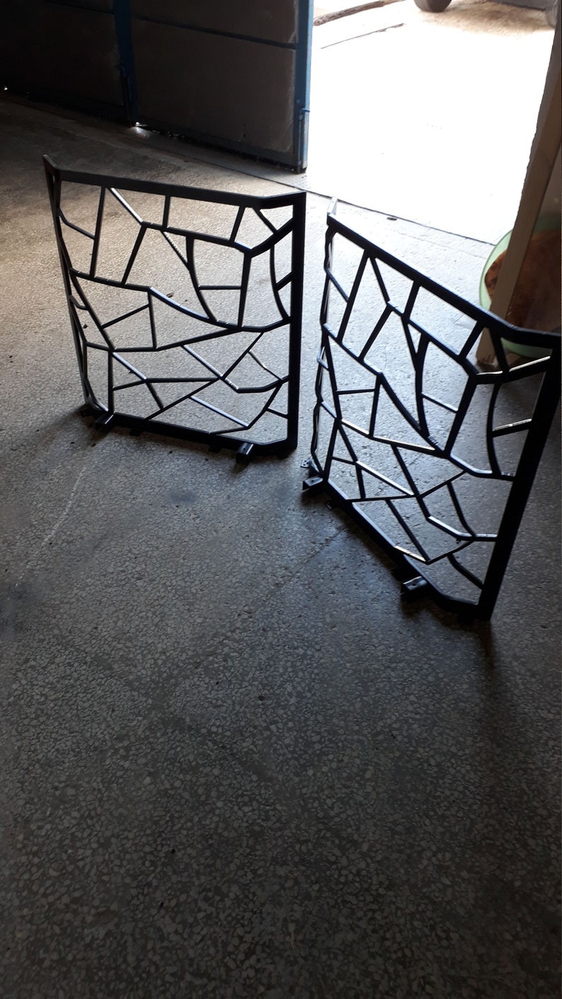 Puede incluir: Dos portales de metal negro con un dise&ntilde;o geom&eacute;trico. Los portales est&aacute;n hechos de finas barras de metal soldadas entre s&iacute; para crear un patr&oacute;n de cuadrados y tri&aacute;ngulos. Los portales est&aacute;n sobre un suelo de hormig&oacute;n.