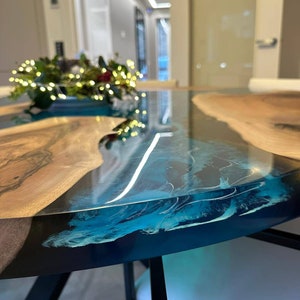 May include: A close-up of a round, wooden table with a blue epoxy resin top. The table has a natural wood edge and black metal legs.