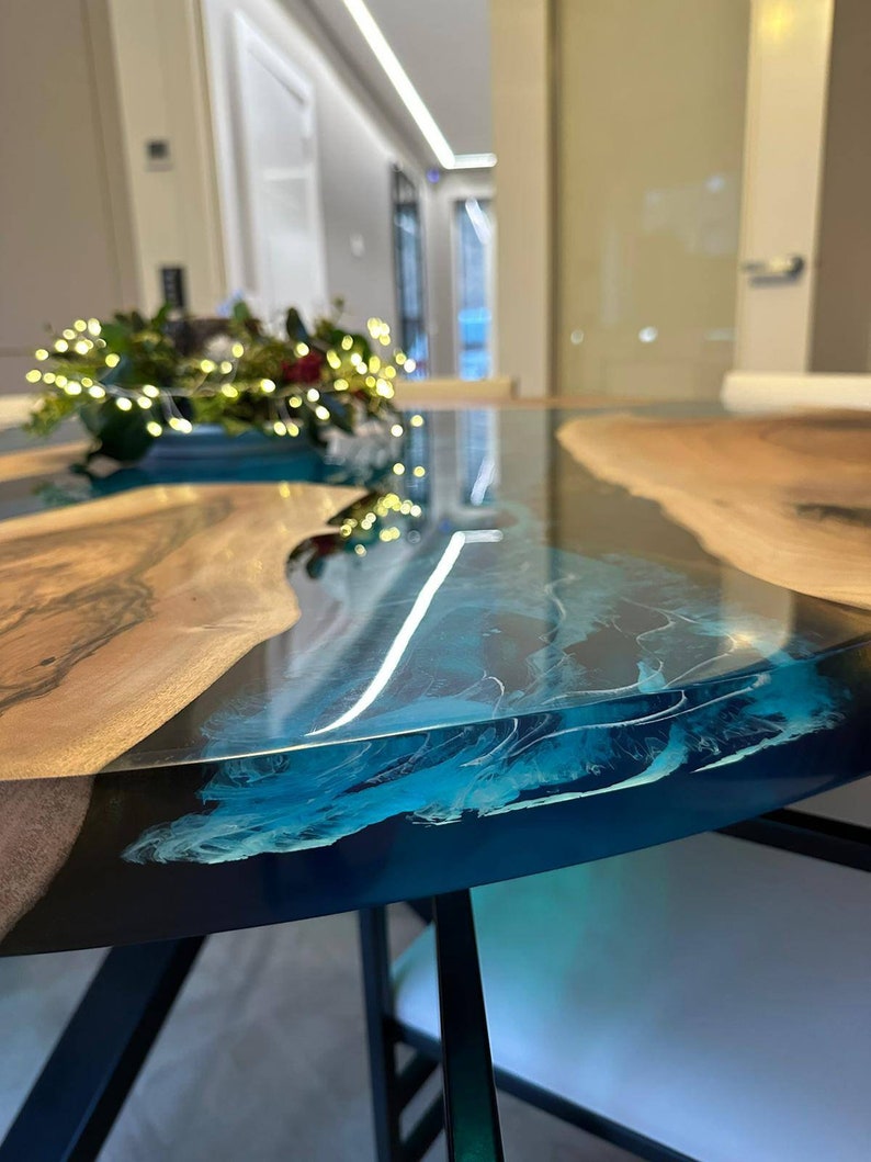 May include: A close-up of a round, wooden table with a blue epoxy resin top. The table has a natural wood edge and black metal legs.
