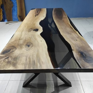 May include: A large wooden dining table with a black epoxy resin river flowing through the center. The table has a black metal X-shaped base.