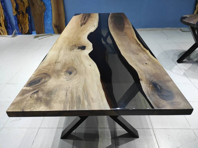 May include: A large wooden dining table with a black epoxy resin river flowing through the center. The table has a black metal X-shaped base.