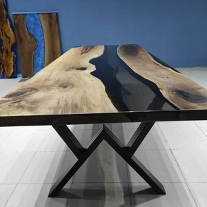 May include: A large wooden dining table with a black epoxy resin river flowing through the center. The table has a black metal X-shaped base.